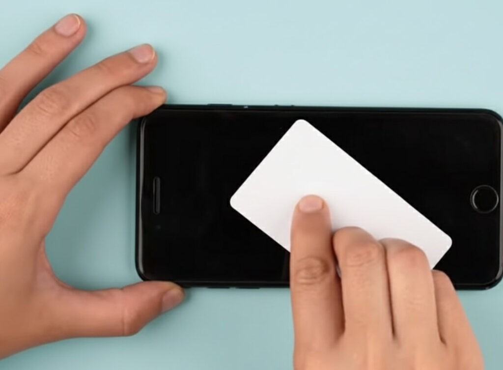 Using a flat card to apply controlled pressure and push an installation bubble toward the screen edge