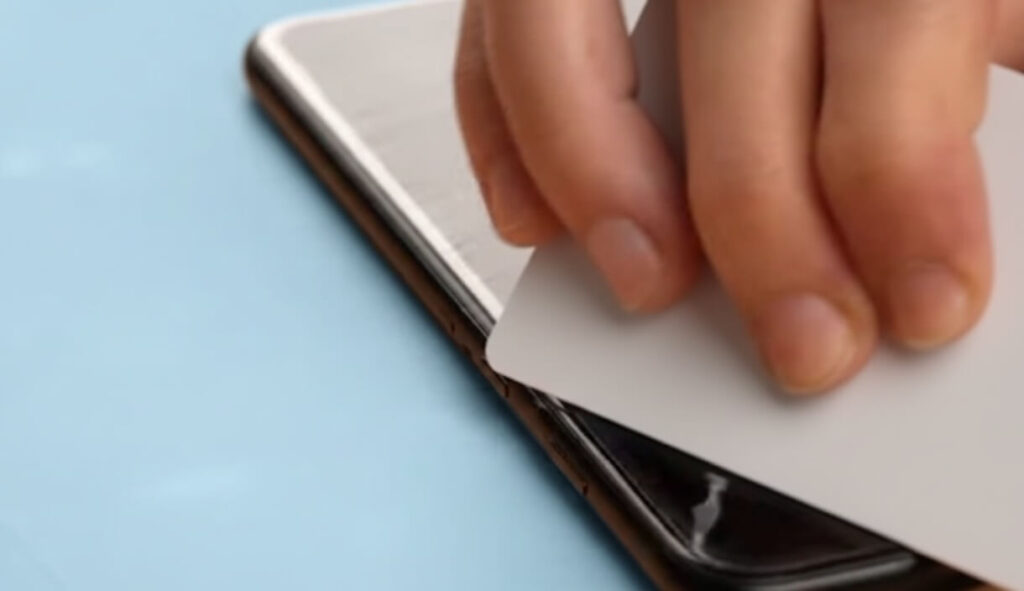 Lifting the edge of a screen protector with a flat card to remove dust trapped between the adhesive and the screen